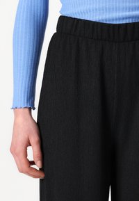 Black textured pants with an elastic waistband, paired with a light blue long-sleeve top featuring ribbed detailing and frayed cuffs.