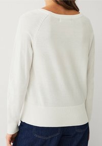 Pull blanc en maille avec un col rond, des manches longues, des poignets et un ourlet à côtes. Texture lisse avec des détails subtils sur les coutures des épaules.