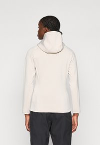 Lichtbeige capuchonjack met een aansluitend ontwerp en lange mouwen. Heeft een hoge kraag en een gladde stoftextuur.