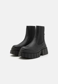 Black faux leather ankle boots with elastic side panels, chunky flatform soles, and a ridged texture. Sleek and modern design.