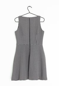 Svartvit mönstrad ärmlös klänning med utsvängd kjol och dragkedja bak, hängande på en svart galge.