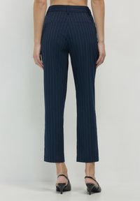 Pantalons à rayures marines avec une taille intermédiaire, des jambes fuselées et des poches arrière, fabriqués en tissu lisse. Chaussures à talons visibles.