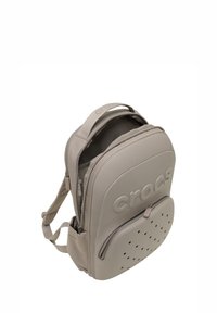 Mochila Crocs gris con superficie texturizada, forma redondeada, cierres de cremallera dobles y bolsillo frontal perforado para ventilación.
