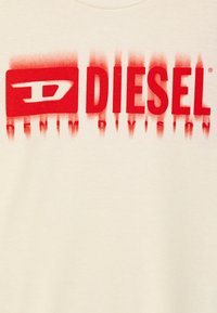T-shirt color crema con una grafica audace in rosso che recita "DIESEL DENIM DIVISION", con un elemento logo rettangolare.