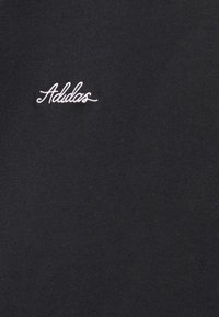 Černá látka s hladkým povrchem, na které je bílé vyšívané logo "Adidas" umístěné blízko vrchní části. Jednoduchý, minimalistický design.