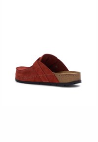 Røde ruskinds slip-on sandaler med justerbar rem, korkfodbed og sort gummisål, vist fra en let højre vinkel på hvid baggrund.