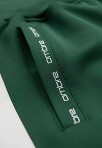 Gröna sportshorts med en slät textur, med en sidoficka med dragkedja. "Ombre"-logotyp i ljusgrått på fickan.