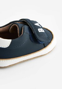 Chaussure pour tout-petit bleu marine avec des accents blancs, en cuir doux, avec une bandoulière en Velcro ajustable et une semelle texturée pour l'adhérence. Détails cousus visibles.