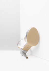 Scarpa con tacco alto argentata, con punta appuntita, design con cinturini e suola beige texturizzata. Presenta sottili accenti luccicanti sui cinturini.