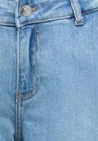 Primer plano de unos vaqueros de mezclilla azul claro que muestran el botón, la cremallera y los detalles de costura.