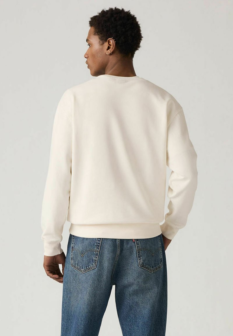Sweat-shirt crème avec un col rond et des poignets côtelés, associé à un jean denim bleu présentant deux poches arrière et une texture délavée.