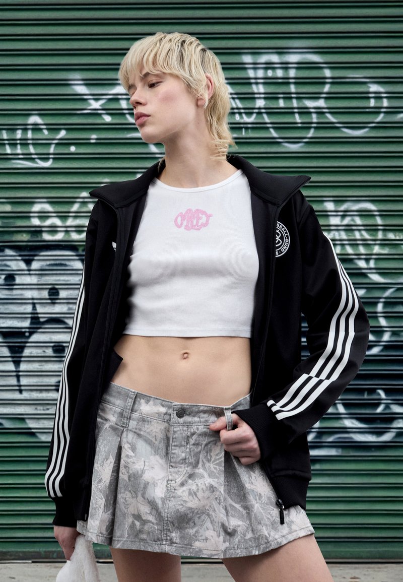 Črna jakna z zadrgo in belimi črtami, beli kratki top in siva mini krilo z vzorcem. Vidni so teksturirani in oprijeti dizajni.