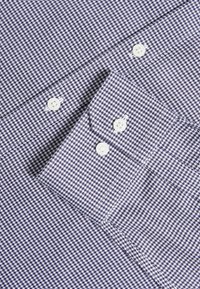 Camicia a quadri blu e bianca con un tessuto testurizzato, colletto classico e bottoni bianchi in plastica con un motivo a contrasto.