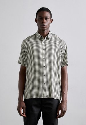 Chemise à manches courtes boutonnée en motif à carreaux noir et blanc, en tissu léger, avec un col classique et des boutons noirs.