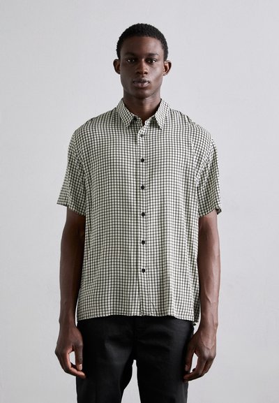 Chemise à manches courtes boutonnée en motif à carreaux noir et blanc, en tissu léger, avec un col classique et des boutons noirs.