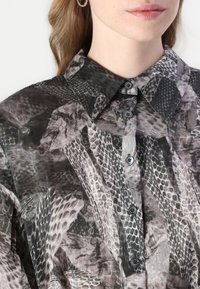 Camicia a maniche lunghe in tessuto trasparente con motivo a pelle di serpente grigio e nero. Include un colletto classico e una chiusura con bottoni sul davanti.