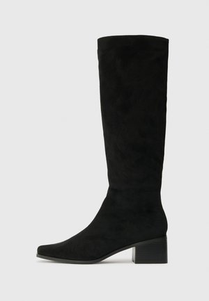 Stivali neri in suede al ginocchio con punta appuntita e tacco quadrato chunky, caratterizzati da una texture liscia e un design minimalista.