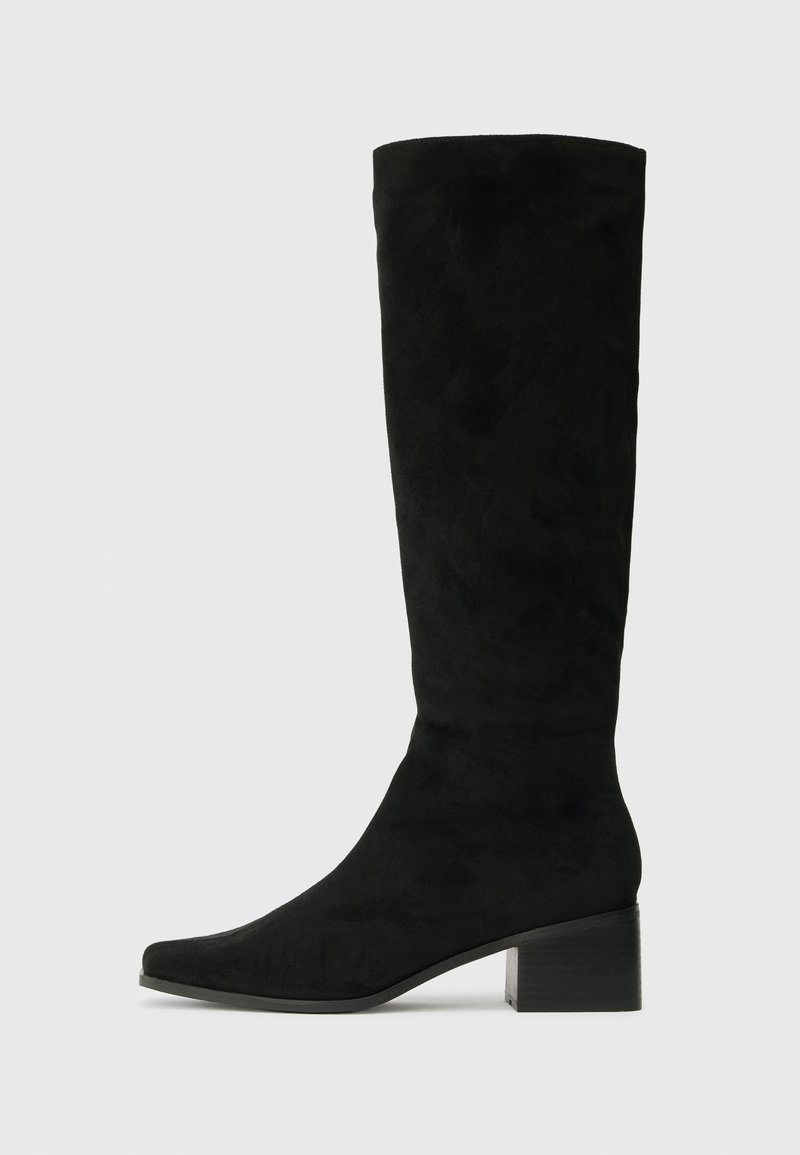 Botas de ante negras hasta la rodilla con puntera puntiaguda y un tacón rectangular grueso, que presentan una textura suave y un diseño minimalista.