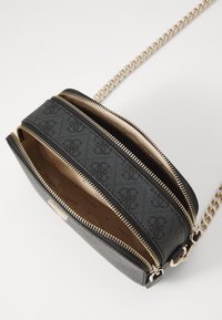 Sac à main noir zippé avec un extérieur texturé, quincaillerie dorée, deux compartiments et une doublure à motifs. Il dispose d'une sangle en chaîne.