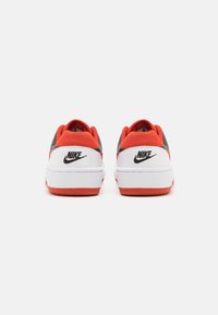 Nike tenisice s bijelom kožnom bazom, crvenim i sivim detaljima, podstavljenim ovratnikom i crnim logotipom na peti. Ravni gumeni potplat.