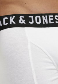 Mutande di cotone bianco con un elastico nero in vita che presenta il marchio "Jack & Jones" in bianco. Il tessuto ha una superficie liscia.