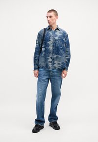 Denim overhemd met een blauw abstract patroon, knoopsluiting aan de voorkant, enkele borstzak. Gecombineerd met blauwe jeans en zwarte schoenen.
