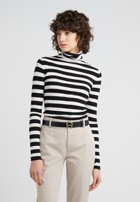 Schwarz-weiß gestreifter Rollkragenpullover aus weichem Stoff, kombiniert mit beigen Hosen und einem schwarzen Gürtel mit einer goldenen Schnalle.