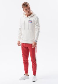 Sudadera blanca con capucha y gráfico "OMG", combinada con joggers rojos ajustados con rayas laterales y zapatillas blancas. Corte Slim.