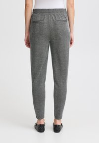Graue Fischgrät-Hosen mit elastischem Bund und zwei Gesäßtaschen. Glatte Textur mit taillierter Beinform. Ein Paar schwarze Ballerinas sichtbar.
