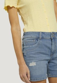 Top giallo a coste con maniche corte e chiusura a bottoni abbinato a pantaloni corti in denim blu chiaro con orlo sfrangiato e dettagli di tasca consumata.