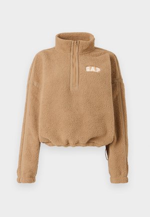 Tan fleece pullover with a half-zip collar, elastic waistband, and side stripe details. Features "GAP" logo in white on the chest.