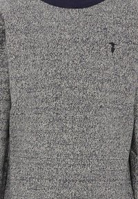 Szary sweter dzianinowy z teksturowanym wzorem, z ciemnoniebieskim okrągłym dekoltem i małym czarnym logo na piersi.