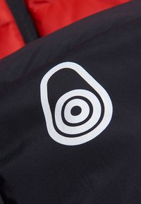 Svart tyg med glänsande yta som har en framträdande vit logotypdesign, som inkluderar koncentriska cirklar och en oval form.