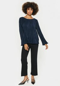 Námornícka plisovaná blúzka s lodičkovým výstrihom a dlhými rukávmi, spárovaná s úzkymi čiernymi nohavicami a čiernymi sandálmi na opätku.