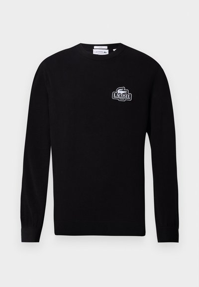 Pull noir à manches longues et col rond avec petit logo blanc Lacoste Paris et emblème de crocodile sur le côté gauche de la poitrine.