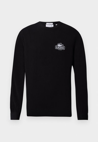 Pull noir à manches longues et col rond avec petit logo blanc Lacoste Paris et emblème de crocodile sur le côté gauche de la poitrine.