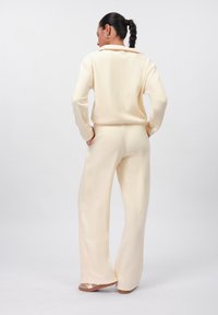 Kremasti, oversized pleteni top s ovratnikom, uparen s širokim hlačama u istoj boji; glatka tekstura, ležeran dizajn.