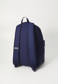 Marineblå ryggsekk med polstret bakstykke og justerbare stropper; har en liten side-lomme og en logo-patch på stroppen.