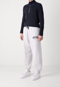 Námořnická polo tričko se zipem spojené se světle šedými tepláky s logem "TOMMY JEANS" a bílými teniskami s černými akcenty.