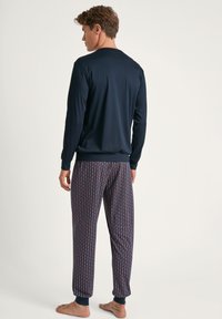 Marineblauw longsleeve shirt met ribgebreide manchetten, gecombineerd met pyjamabroek met een herhalend geometrisch patroon in bordeauxrood en blauw.