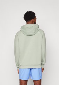 Lys grønn hettegenser med en avslappet passform, med snøring i hetten og ribbestrikkede mansjetter, sammen med blå shorts. Myk tekstur, minimalistisk design.