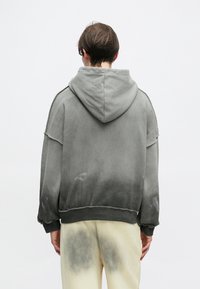 Γκρι φούτερ με φθαρμένο εφέ ombre, διαθέτοντας κουκούλα με κορδόνια, ραμμένες μανσέτες και φθαρμένες λεπτομέρειες. Φορεμένο με ανοιχτόχρωμο παντελόνι.