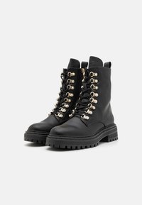 Bottines en cuir noir avec une semelle épaisse, œillets en finition dorée et lacets. Présente une texture réussie et un col rembourré pour le soutien.
