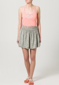 Koraalkleurige tanktop met kanten details bij de halslijn, gecombineerd met een lichtgrijze rok met een subtiele patroondesign. Oranje sandalen met witte bandjes.
