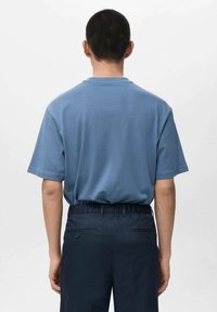 Krótki rękaw, koszulka z okrągłym dekoltem w jasnoniebieskiej bawełnie. Noszona z ciemnogranatowymi spodniami z elastycznym pasem i bocznymi kieszeniami.