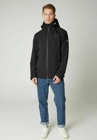 Czarna wodoodporna kurtka z wysokim kołnierzem, regulowanym kapturem i zapięciem na zamek. Połączona z podwiniętymi niebieskimi dżinsami i białymi trampkami.
