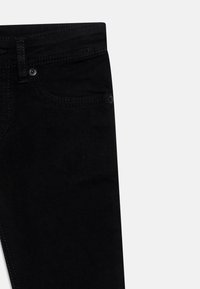 Vaqueros de denim negro que muestran la sección superior del frente con la presilla del cinturón, el bolsillo delantero y costuras visibles sobre un fondo blanco.