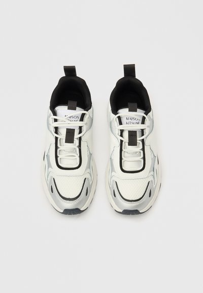 Λευκά και ασημί αθλητικά παπούτσια με πλέγμα και συνθετικές επιφάνειες, μαύρες λεπτομέρειες, ταινία έλξης στη φτέρνα και ορατά κορδόνια με λογότυπο στη γλώσσα.