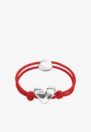 Bracelet double corde rouge avec un pendentif en forme de cœur argenté brillant et une fermeture ovale, noué avec des nœuds visibles près du pendentif.