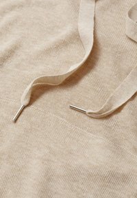 Tela de algodón beige con una textura suave, con cordones planos con puntas metálicas y costuras visibles a lo largo de la superficie.